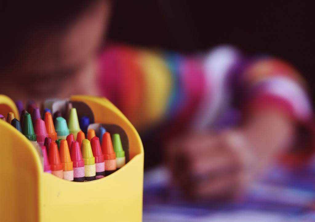 Crayons in the foreground with a girl blurred in the background coloring.