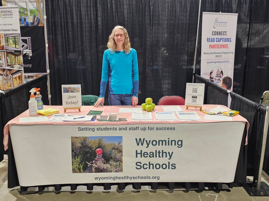 A table with a Wyoming Healthy Schools banner on the front of it and a woman standing behind it.